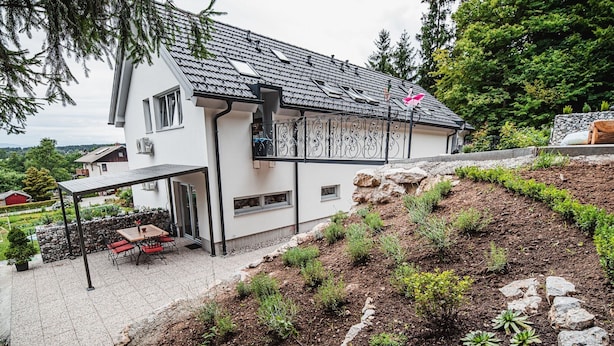 Ein modernes Haus mit Satteldach, überdachter Terrasse und einem angelegten Garten mit Steinen und Pflanzen.