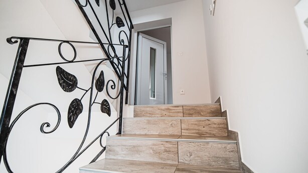 Een trap met een zwarte metalen balustrade met bladmotieven, die naar een deur leidt.