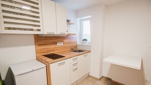 Een kleine keuken met witte kastjes, een houten aanrecht, een inbouwoven en een raam met uitzicht.