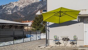 Een terras met een gele parasol, twee stoelen en een tafel, met uitzicht op een besneeuwde berg.