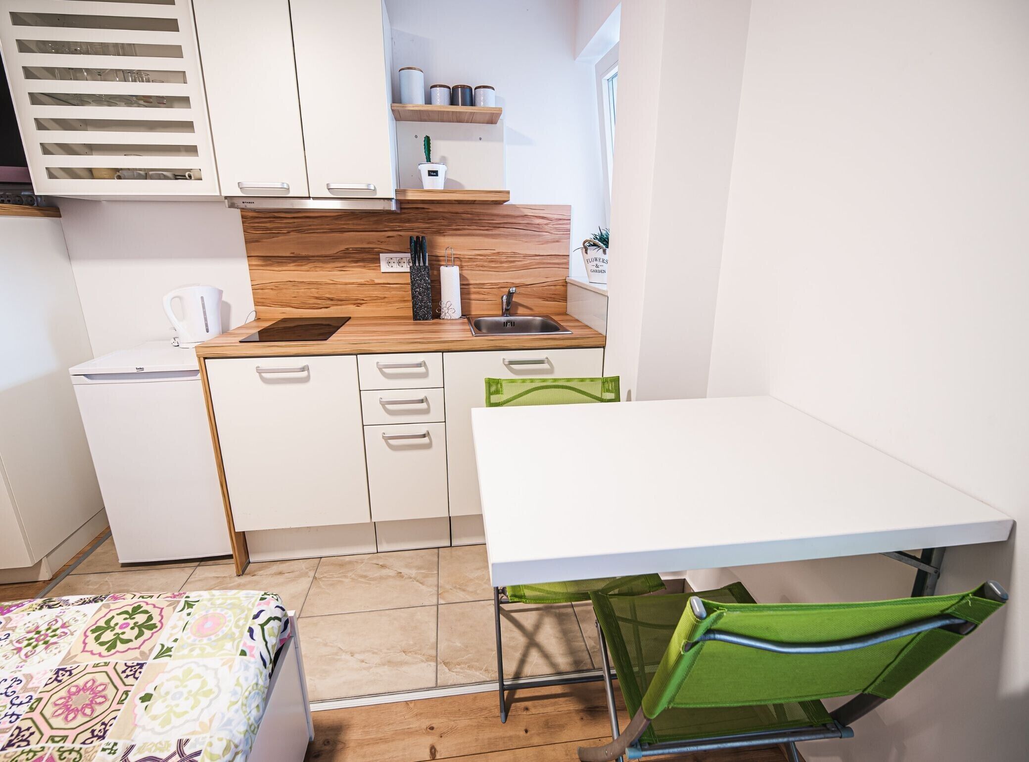 Pieni, käytännöllinen keittiö, jossa on valkoiset kaapit, puinen työtaso, pesuallas ja pieni jääkaappi.