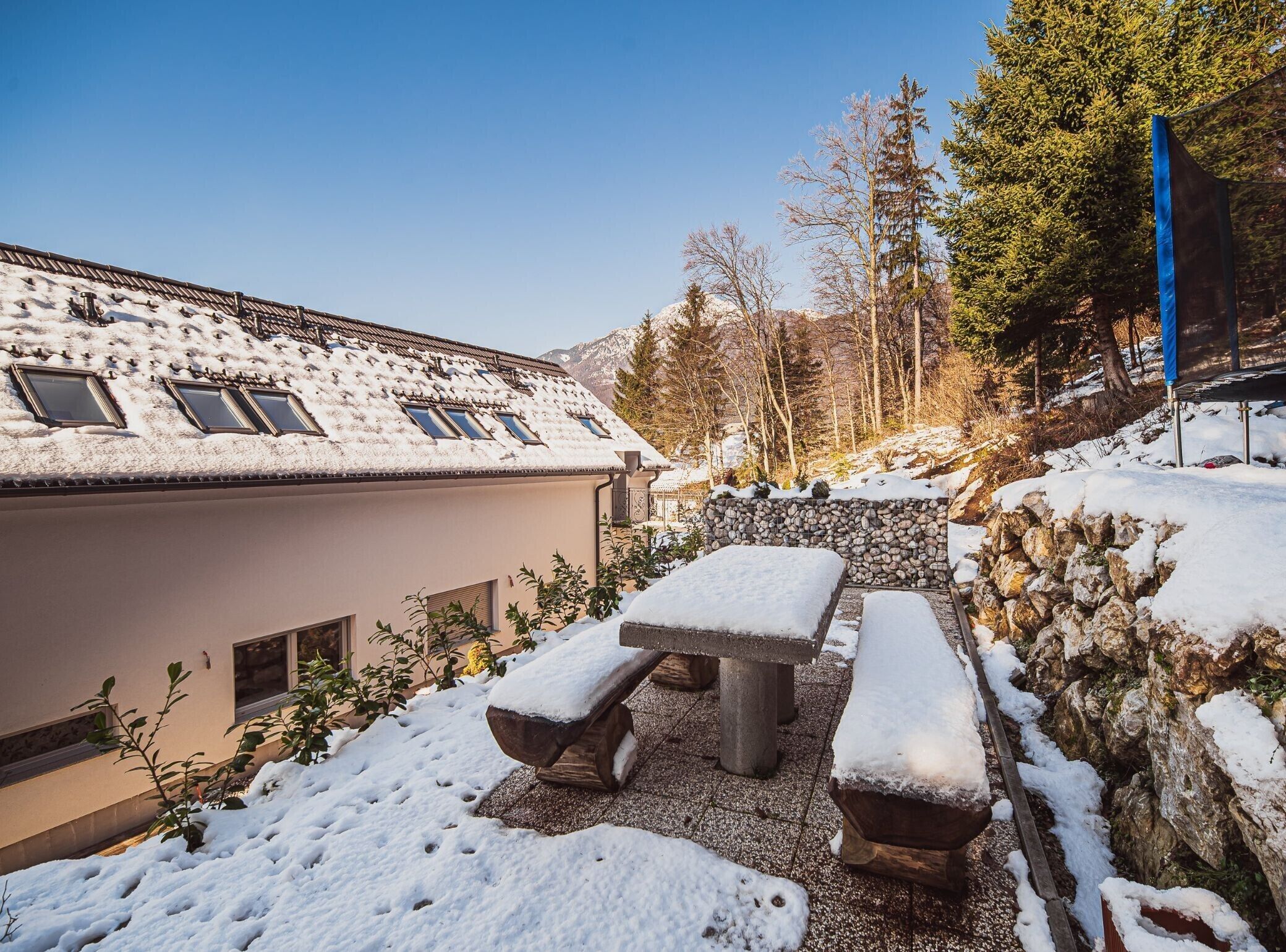 A snow-covered outdoor area with a stone wall, a wooden bench, and a picnic table.