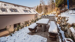 A snow-covered outdoor area with a stone wall, a wooden bench, and a picnic table.