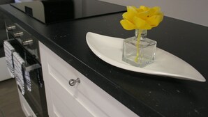 Un comptoir de cuisine sur lequel repose une assiette blanche, et sur laquelle se trouve un flacon en verre contenant des fleurs jaunes.