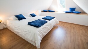 A bedroom with a large bed, a window seat with pillows, and a wooden floor.