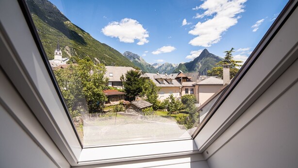 Vista dalla finestra su una zona residenziale con case, una chiesa e montagne.