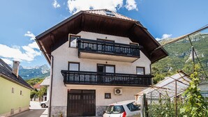 Un edificio a due piani con un balcone, un'auto parcheggiata di fronte e montagne sullo sfondo.