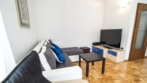 Un ambiente compatto con un divano, un piccolo tavolo, una televisione e un mobile.