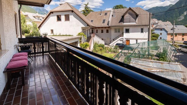 Un balcone con pavimento in legno e un cuscino rosa, con vista su una zona residenziale con case e montagne sullo sfondo.