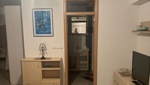 Quarto com escrivaninha de madeira, televisão, espelho e quadro na parede.