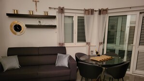 Un salon avec un canapé marron foncé, deux fauteuils noirs, une table en verre et une horloge murale.