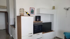 Une cuisine compacte équipée d’un four encastré, d’un four à micro-ondes et d’une machine à café posée sur le plan de travail.