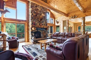 Interno di una baita in legno con camino in pietra, mobili in pelle e un'ampia finestra vista sulla foresta.