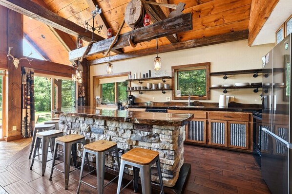 A rustic kitchen with a stone island, wooden bar stools, and a large refrigerator. - Big Woods and Yellow River (Necedah)