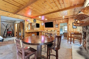 Un interno rustico in legno con un tavolo rotondo, angolo bar e parete in pietra.
