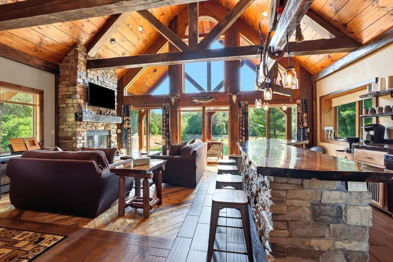 A spacious living area with a stone fireplace, wooden beams, and a large window overlooking greenery.