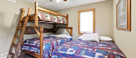 Une chambre avec un lit superposé, une échelle, un ventilateur de plafond et une fenêtre avec des stores.