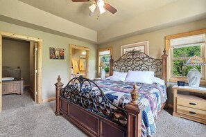 A bedroom with a large bed, a wooden headboard, a nightstand, a lamp, and a window with a view of greenery. - Big Woods and Yellow River (Necedah)