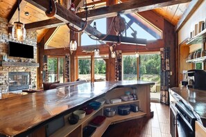 A rustic kitchen with a stone fireplace, wooden beams, and a large island with storage shelves.