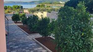 Ein gepflasterter Weg führt zu einem Balkon mit Blick auf ein Gewässer, umgeben von Grün und einer entfernten Hügellandschaft.