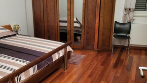 Ein Schlafzimmer mit einem hölzernen Bett, einem Kleiderschrank, einem Stuhl und einem Fenster mit Vorhängen.