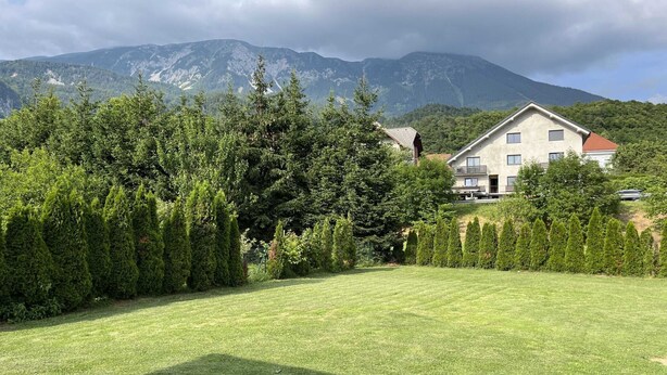 A well-maintained lawn with a building in the background, surrounded by trees and mountains.