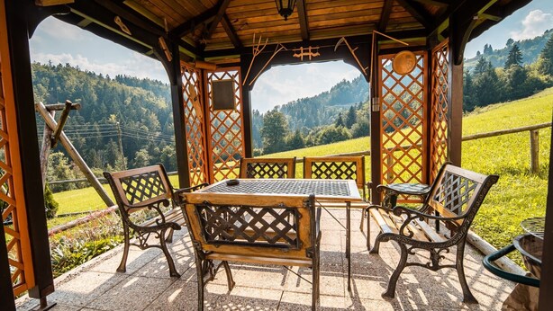 Un mirador de madera con una mesa y sillas, con vistas a un paisaje pintoresco con colinas y árboles.