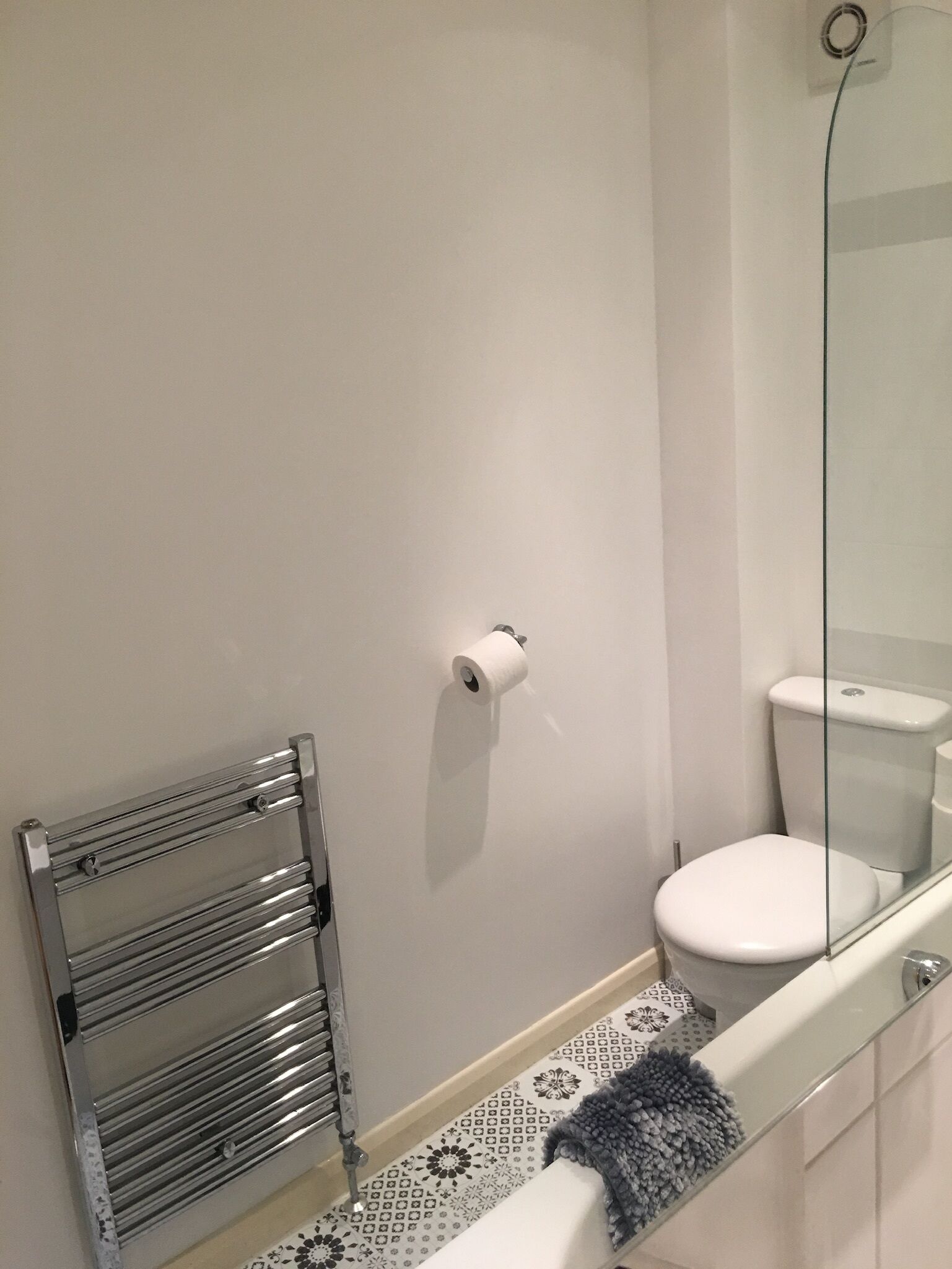 A bathroom with a toilet, a glass shower enclosure, a towel rack, and a toilet paper holder on the wall.
