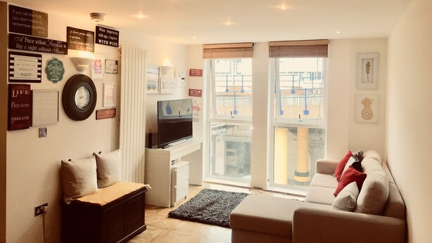 A cozy living room with a sofa, a small table, a TV, and a window with a view of a building. - Charming spacious 2 bed apartment  (London)