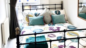 A bedroom with a bed, a window with curtains, a radiator, and a hanging light fixture. - Charming spacious 2 bed apartment  (London)