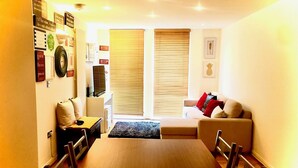 A dining area with a wooden table and chairs, a sofa with cushions, and a television on a stand. - Charming spacious 2 bed apartment  (London)