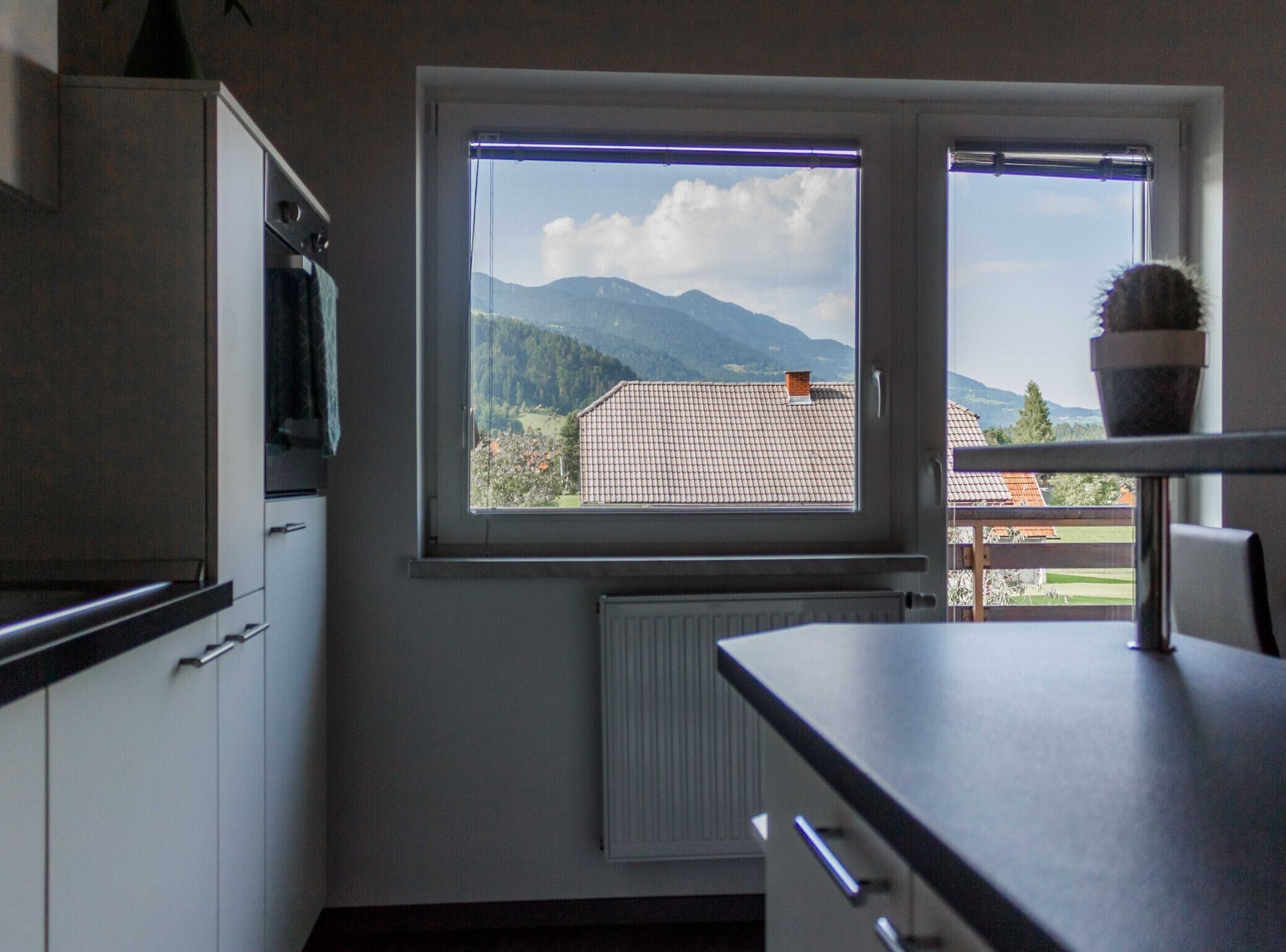 A kitchen with a window view of a mountain and a house.