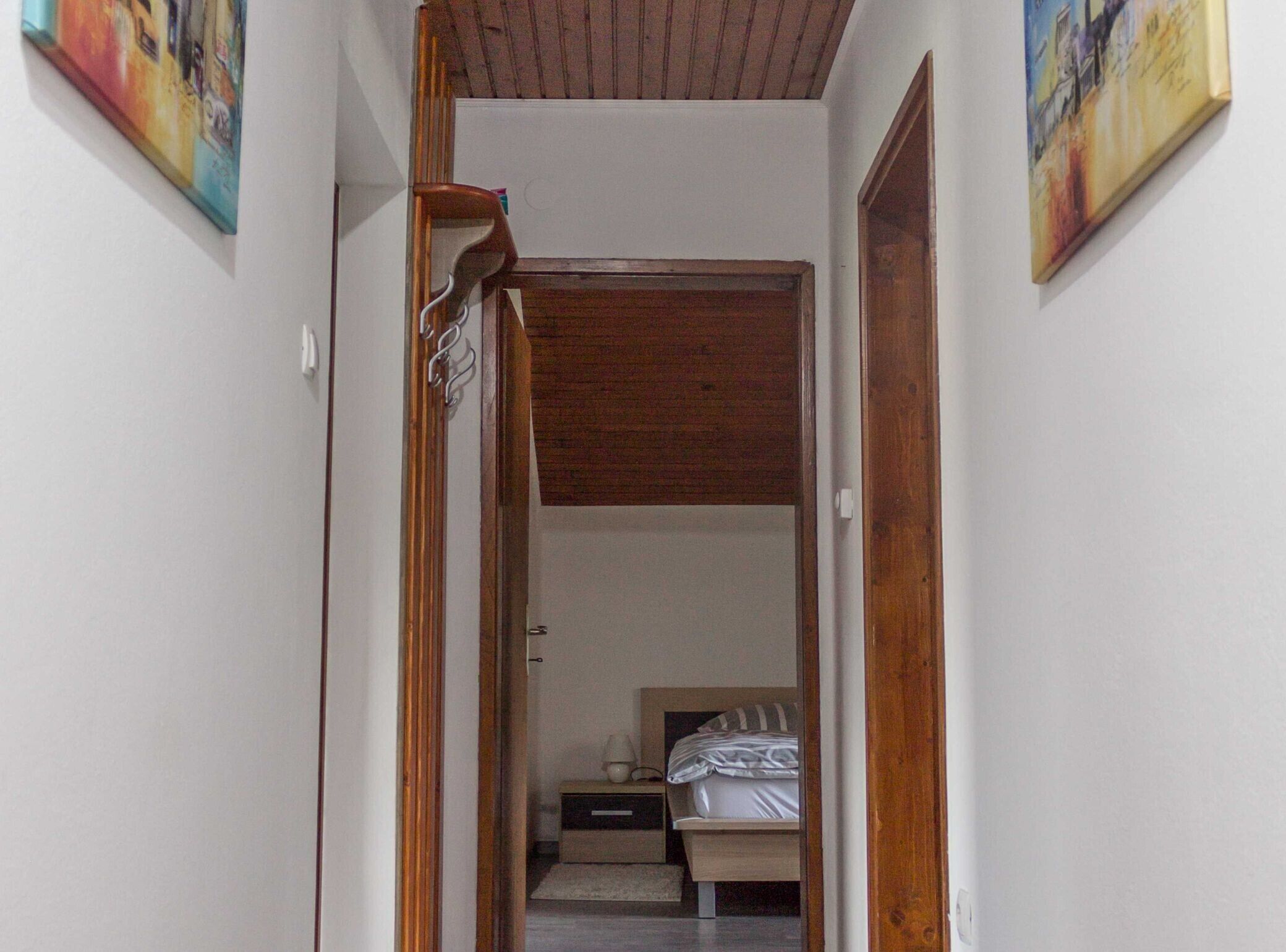 A narrow hallway leading to a bedroom with a bed and nightstand.