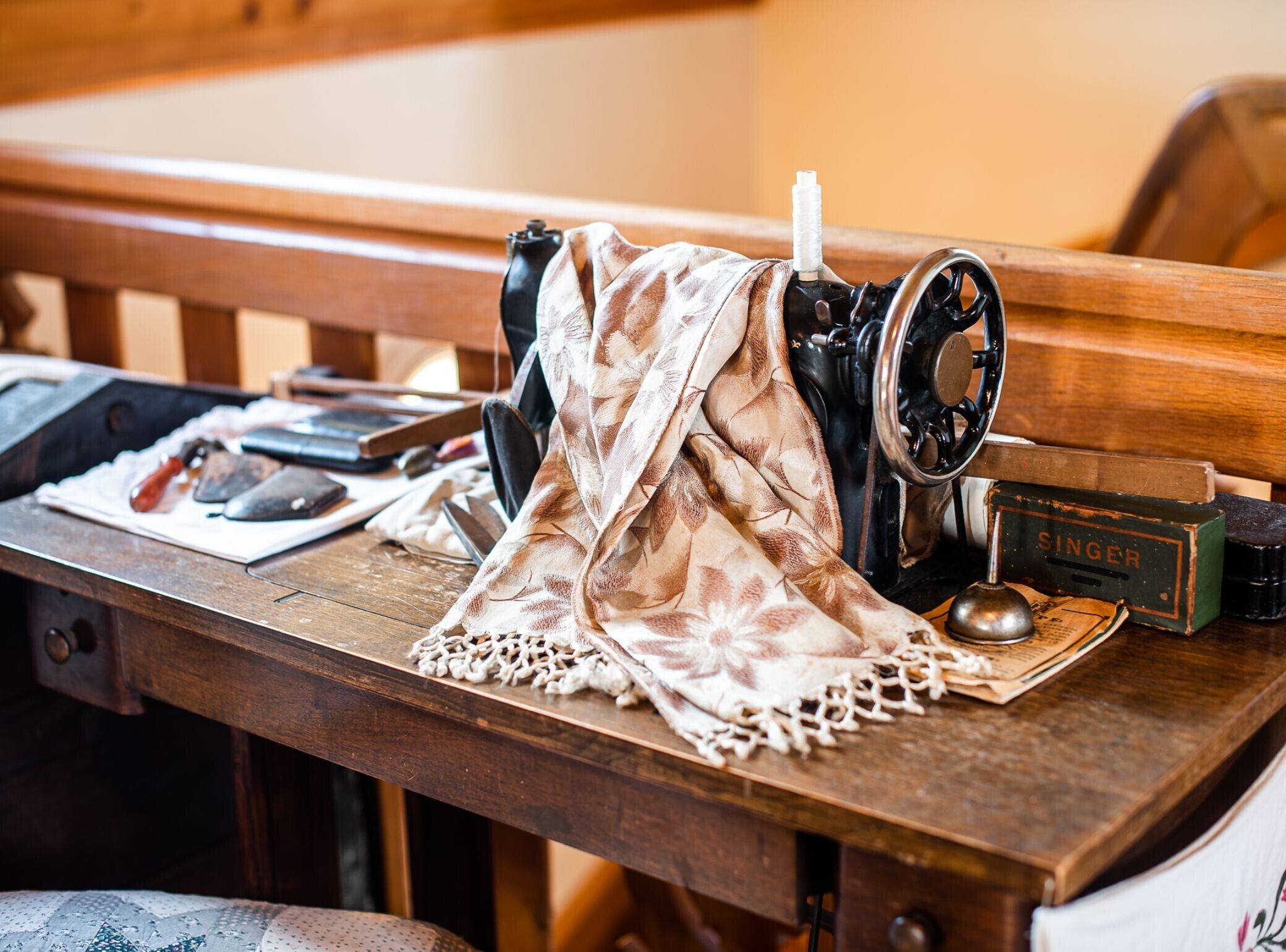 Une machine à coudre Singer ancienne, posée sur une table en bois, avec un tissu à motifs et une cuillère.