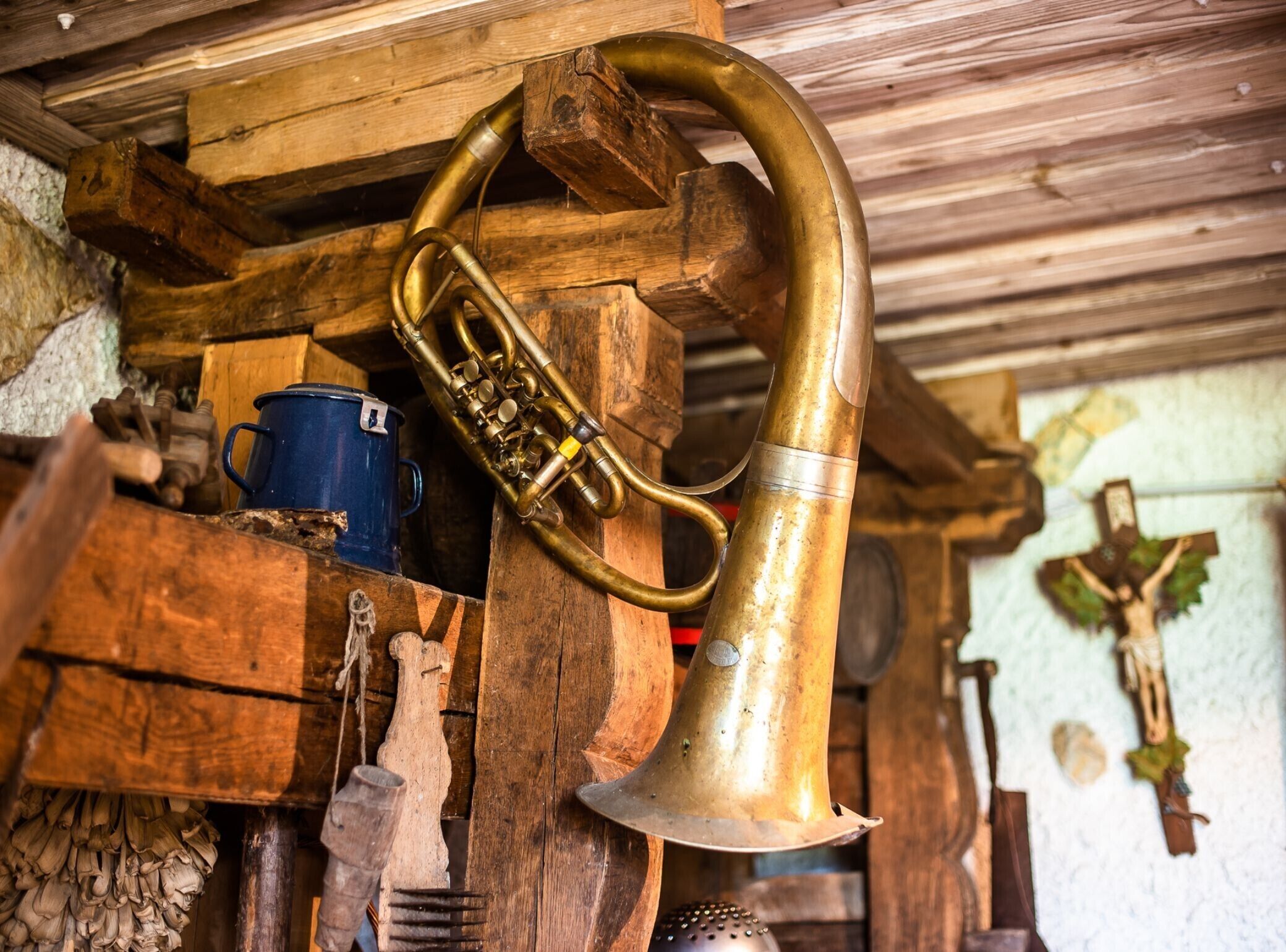 A rustic interior with a wooden structure, a brass bell, and a wooden cross on the wall.