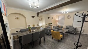 A dining area with a marble table, grey upholstered chairs, and a yellow chair. There are sofas and a floor lamp in the living area. - 3BR House with Free WiFi All Over UK (London)