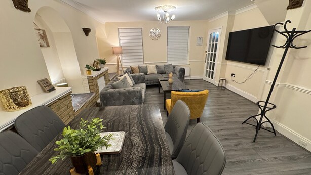 A living room with a sofa set, a dining table with chairs, a TV mounted on the wall, and a floor lamp. - 3BR House with Free WiFi All Over UK (London)