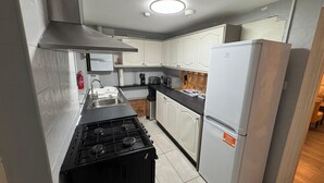 A modern kitchen with a gas stove, stainless steel sink, white cabinets, and a white refrigerator. - 3BR House with Free WiFi All Over UK (London)