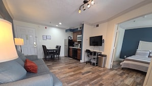 A living room with a sofa, a dining table, a kitchen area, and a bedroom with a bed. - Disney Family Condo Heated Pool (Kissimmee)