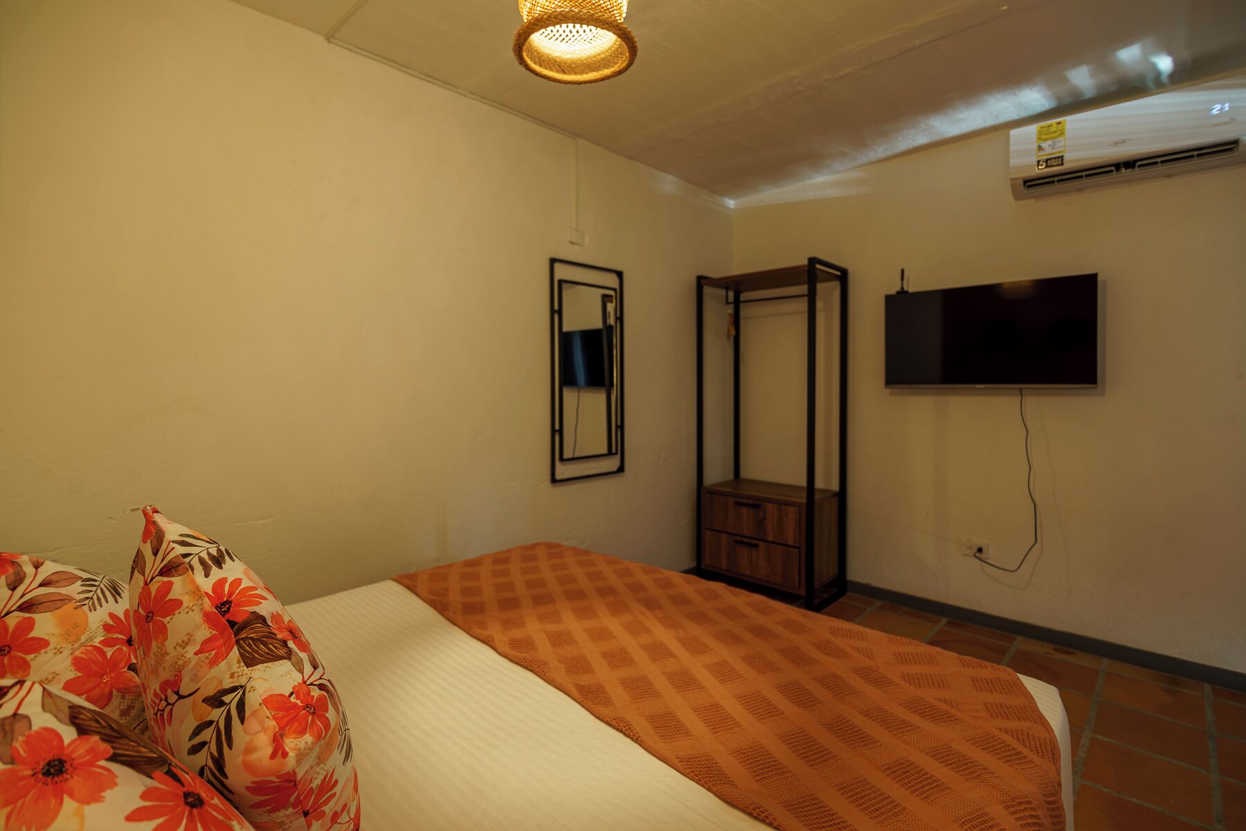 Quarto com cama, mesa de cabeceira, espelho, guarda-roupa e televisão na parede.