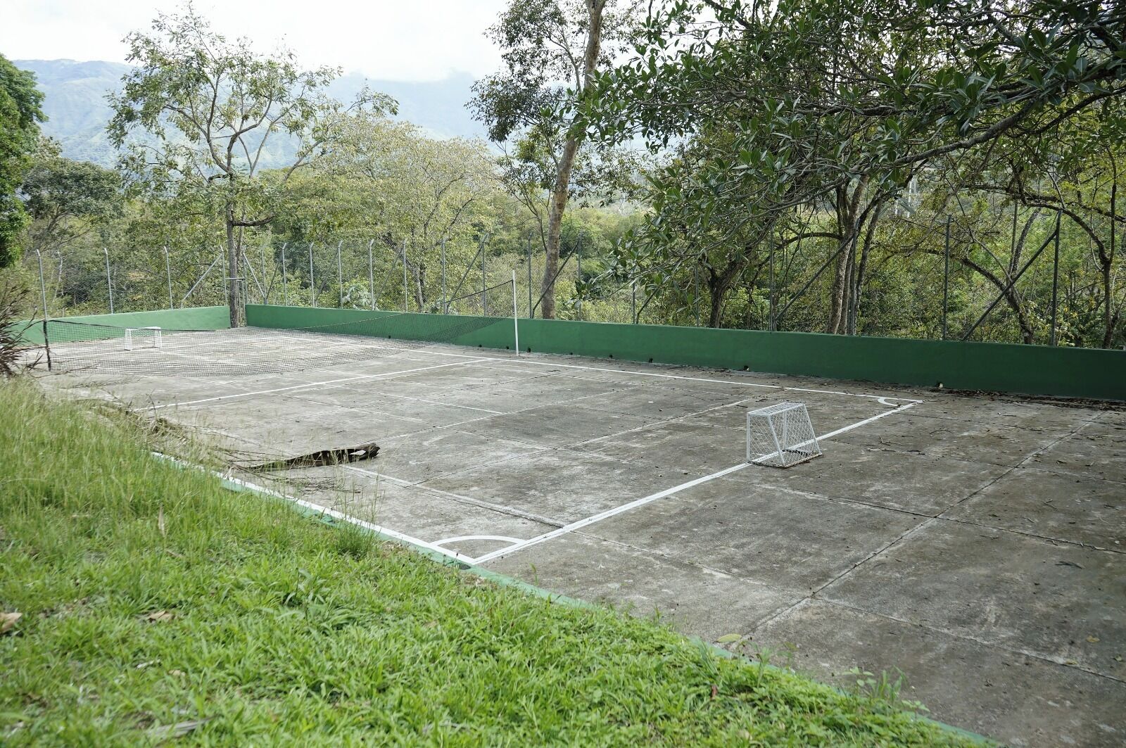 An outdoor tennis court surrounded by trees and a green fence.