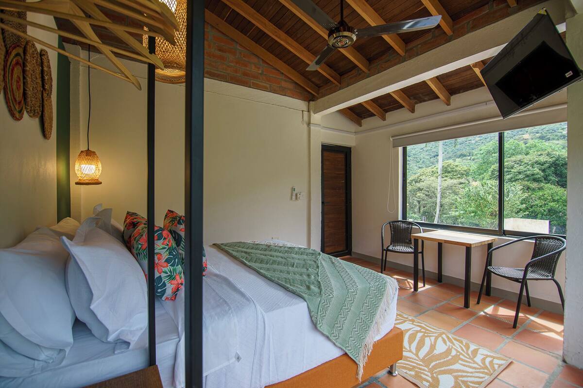 A bedroom with a bed, a TV, a balcony with a table and chairs, and a view of the outdoors.
