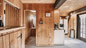A wooden interior with a kitchen area, a refrigerator, and a window.