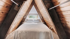 A cozy attic bedroom with a bed centered under a triangular wooden ceiling.
