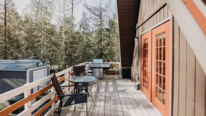 A wooden deck with a barbecue grill, a table with chairs, and a glass enclosure.