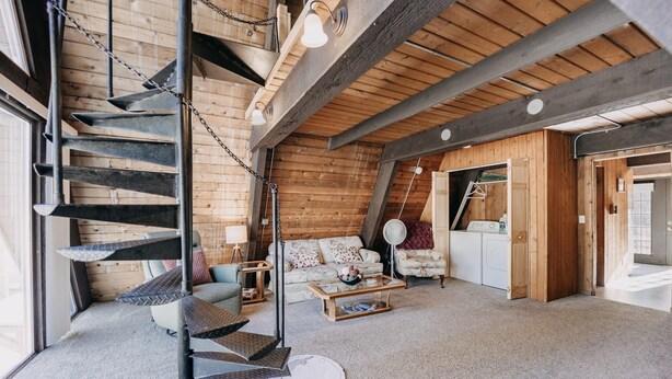 A spacious loft-style room with a spiral staircase, a sofa set, a coffee table, and a washing machine.