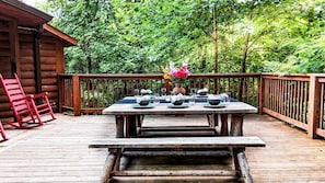 Eine Holzterrasse mit Picknicktisch, gedeckt für ein Essen, umgeben von einem Holzzaun und dichtem Grün.