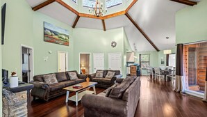 Ein geräumiges Wohnzimmer mit hoher Decke und Holzbalken, ausgestattet mit zwei Sofas, einem Couchtisch und einem Kamin.