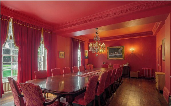 A formal dining room with a long table, red chairs, and a chandelier.