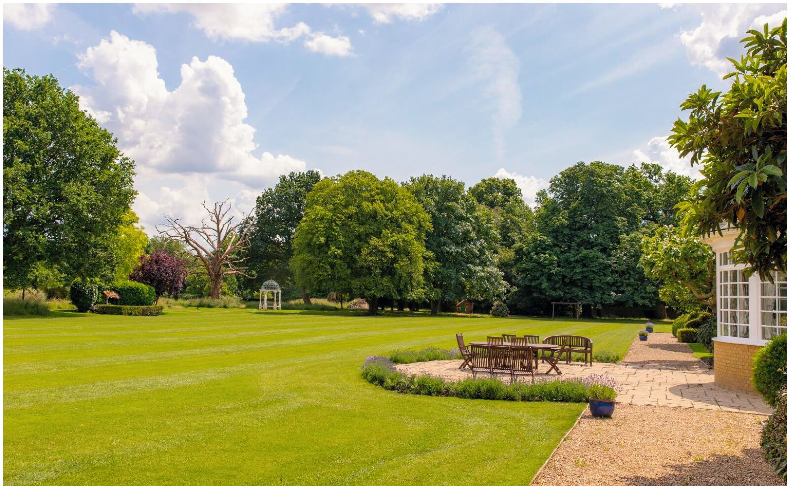 A well-maintained garden with a gazebo, a patio with outdoor furniture, and a variety of trees and shrubs.